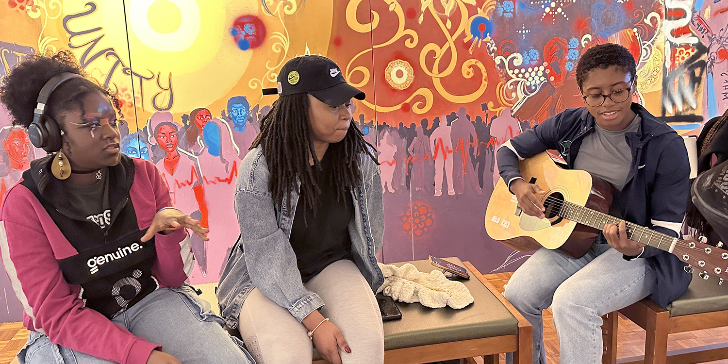 Three students talking and playing guitar in gallery Three students talking and playing guitar in gallery