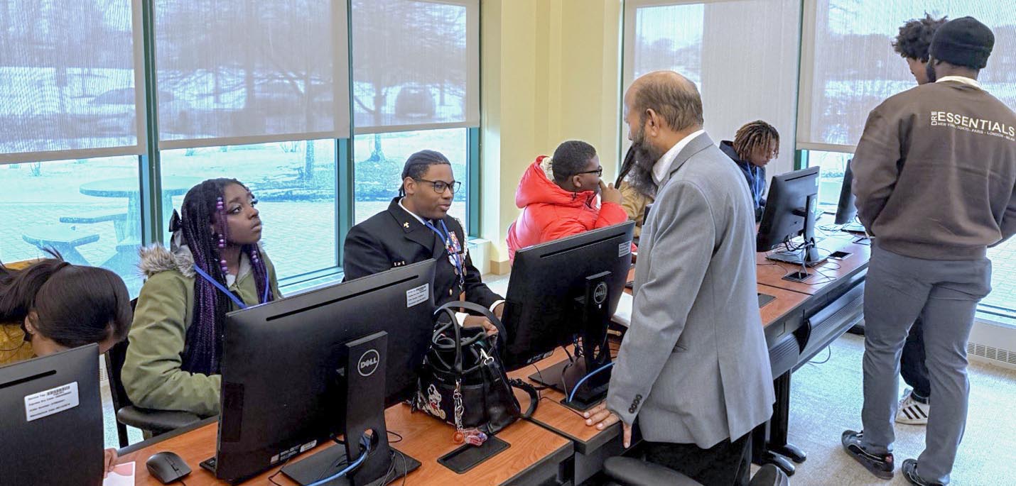 Six students sitting at computers while listening to a professor