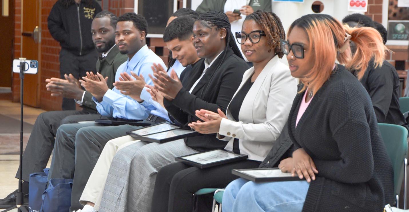 A side-angle photo of Chicago State ComEd scholarship recipients sitting in a row and clapping during the ceremony.
