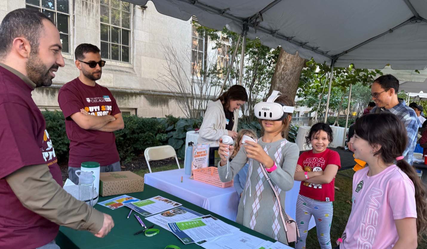 A CIMST student volunteer smiles and looks on as children gather to try a virtual reality headset.