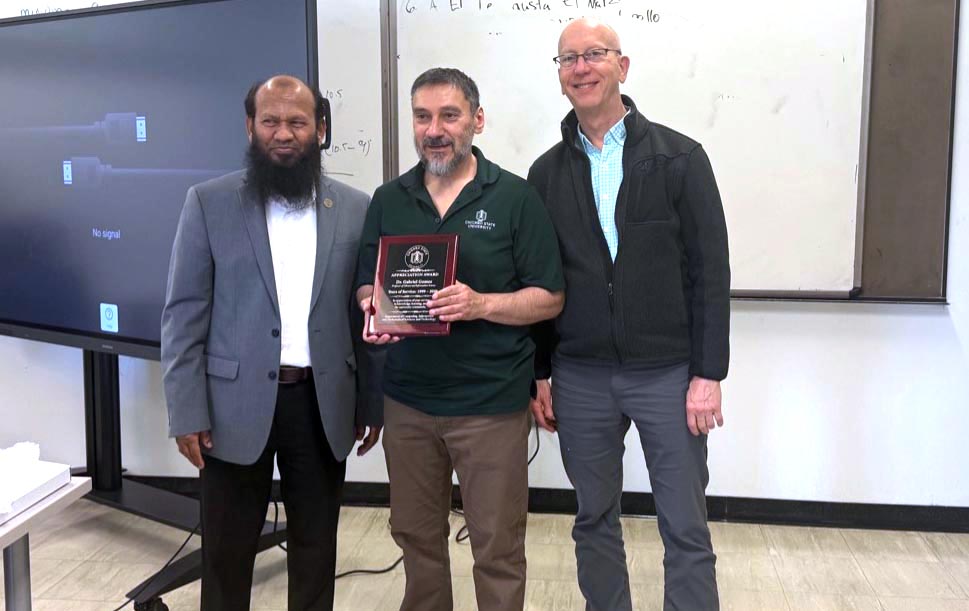 Dr. Gomez smiles while holding a plaque while CIMST chair Dr. Salam and Dean Mark Smith (College of Arts and Science) smile and stand alongside him.