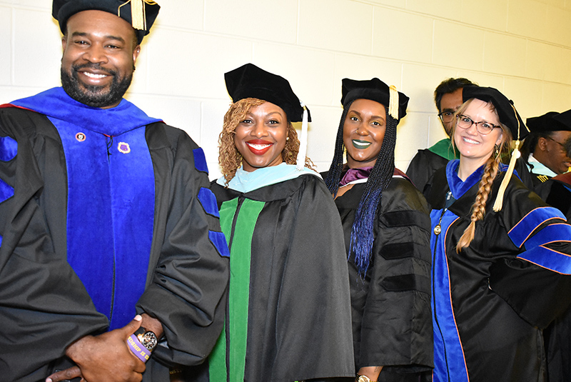 Four Chicago State University faculty marshals dressed in commencement regalia smile together as they prepare for commencement.