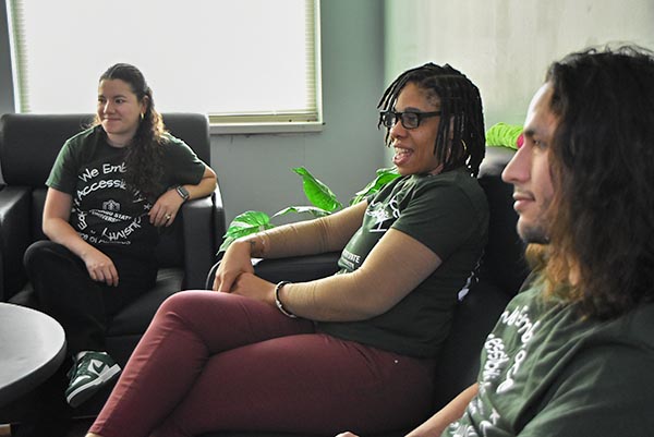 Three people sit and talk casually on a couch