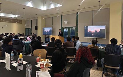 A man speaking at a podium to a large audience seated at round tables in a brightly lit room.