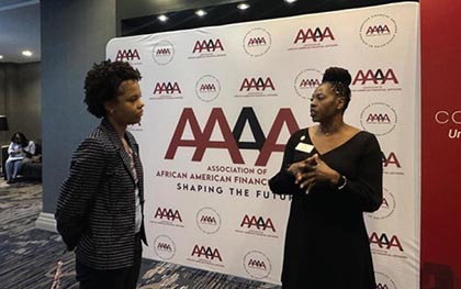 Lisa Pratt, Executive Director of the CWE, talks to a student in front of a backdrop for the "Association of African American Financial Advisors (AAAA).