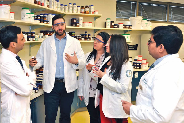 4 people in lab coats listening to a speaker