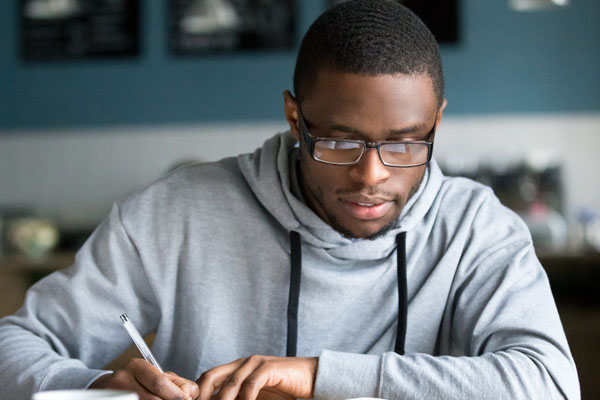 Student in grey hoodie studying and writing notes
