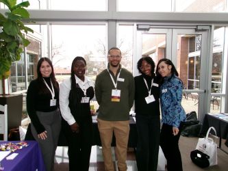 Four professionally dressed students stand alongside Occupational Therapy chair Dr. Luther King&nbsp;(centered)&nbsp;in front of&nbsp;a large window