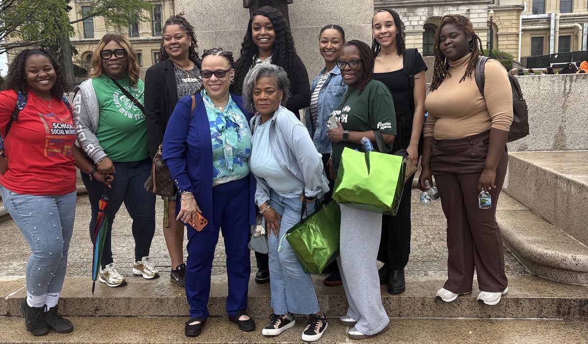 A group of 10 women gather for a group photo on concrete steps in front of a statue at the Illinois State Capitol in Springfield, IL.